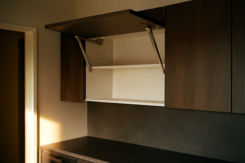 کابینت بالای آشپزخانه با درب بالارونده باز و نگهداشتهشده توسط جک گازی