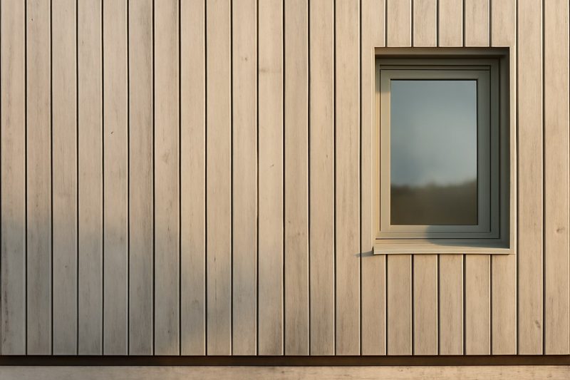 نمای نزدیک نمای چوبی مدرن یک ساختمان با باتنهای عمودی و فاصلهٔ سایه در پایین کار نشاندهندهٔ تهویهٔ پشت نما